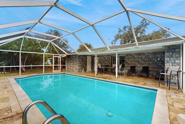 A swimming pool with a glass enclosure, stone walls, and outdoor furniture.
