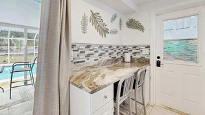 A kitchen with a marble countertop, white cabinets, a dining area with chairs, and a pool visible through a glass door. - Relax, Swim & Explore! A Dog-Friendly Private Pool Retreat Close to Everything! (Port Charlotte)