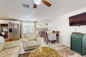 A modern kitchen with stainless steel appliances, a dining area with a table and chairs, a sofa, and a TV mounted on the wall.