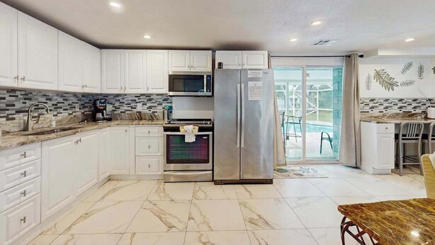 A modern kitchen with white cabinets, a stainless steel refrigerator, a microwave, and an oven. - Relax, Swim & Explore! A Dog-Friendly Private Pool Retreat Close to Everything! (Port Charlotte)