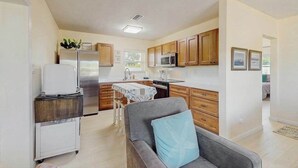 Cocina compacta con armarios de madera, refrigerador, microondas y comedor con mesa y sillas.