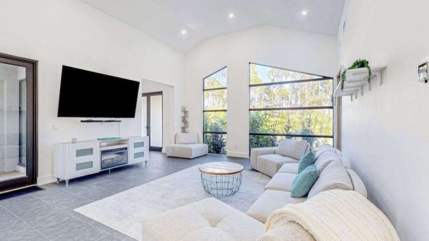 A modern living room with a large flat-screen TV, a sofa, a coffee table, and a large window. - Custom-built home with private patio, central AC, & W/D - dog-friendly (Port Charlotte)