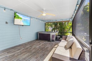 Ein überdachter Patio mit Fernseher, Deckenventilator, Whirlpool und Sitzgelegenheiten im Freien.