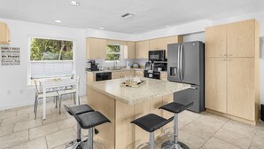 A modern kitchen with a central island, bar stools, a dining table, and a refrigerator. - Spacious coastal Pet friendly home close to beaches and shopping. (Port Charlotte)