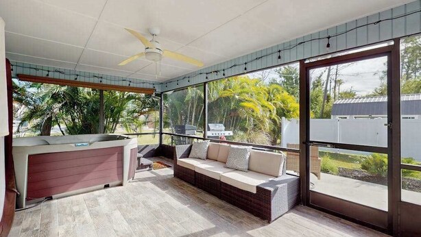 A covered outdoor seating area with a sofa and a table, large windows, and a ceiling fan. - Spacious coastal Pet friendly home close to beaches and shopping. (Port Charlotte)