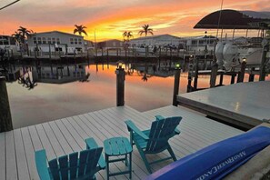 A marina with boats docked, a wooden deck with chairs, and a sunset in the background. - Dog-friendly, canal-front getaway with a dock, screened lanai, & washer/dryer (Saint James City)