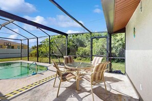 An outdoor patio with a pool, a round table with chairs, and a glass enclosure. - Family and dog friendly pool home, close to beaches, harbor and river (Port Charlotte)