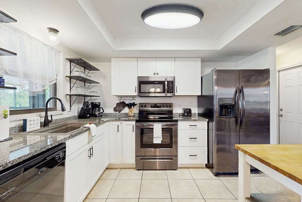 A modern kitchen with white cabinets, stainless steel appliances, a built-in oven, and a refrigerator.