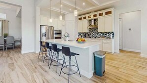 Una cucina moderna con isola centrale, sgabelli da bar, frigorifero in acciaio inossidabile e zoccolo di piastrelle.