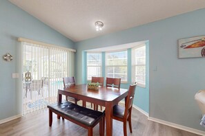 A dining room with a wooden table, chairs, and a bench. There are windows with blinds, a ceiling light, and a door leading outside. - Coastal Cottage with private pool, lanai, and free internet (Port Charlotte)