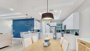 A modern kitchen with white cabinets, a blue accent wall, and pendant lighting. - Well appointed new home with private pool, large yard, W/D & dog friendly (Rotonda West)
