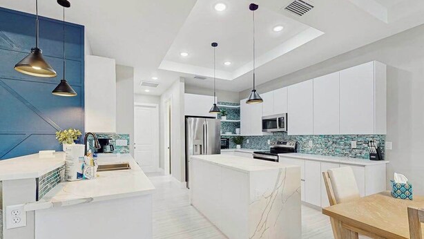 A modern kitchen with white cabinetry, a marble island, pendant lighting, and a backsplash with blue tiles. - Well appointed new home with private pool, large yard, W/D & dog friendly (Rotonda West)