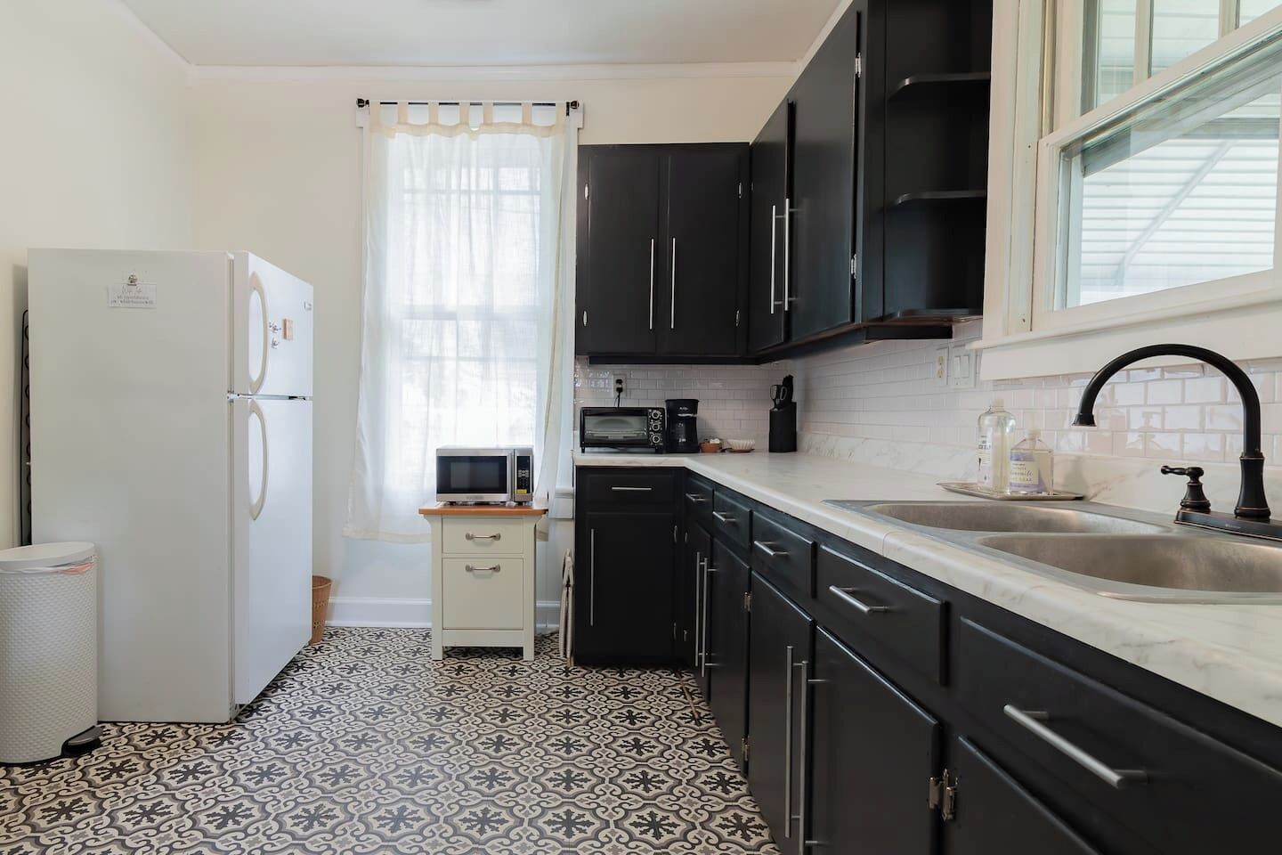 A compact kitchen with a refrigerator, microwave, sink, and black cabinets.