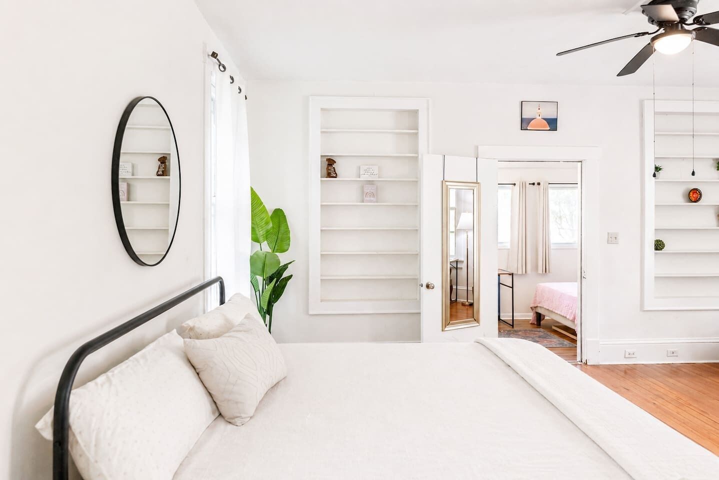 Une chambre à coucher comprenant un lit, un ventilateur de plafond, un miroir et une porte donnant sur une autre pièce.