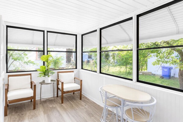 A room with a wooden floor, white walls, and a large window. There are two chairs and a small table.