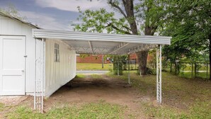 A covered outdoor area with a white building, a dirt path, and a tree. - Casa Blanca|Near Ft Benning|Pet Friendly|King Bed (Columbus)
