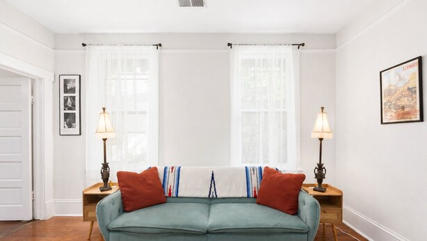 A living room with a teal sofa, two side tables with lamps, a door, and a framed picture on the wall. - Casa Blanca|Near Ft Benning|Pet Friendly|King Bed (Columbus)