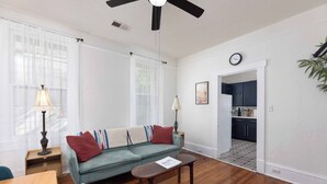 A living room with a sofa, a coffee table, and a dining table. There is a kitchen visible through an open doorway. - Casa Blanca|Near Ft Benning|Pet Friendly|King Bed (Columbus)