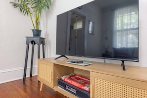 Un mueble de madera con un centro de entretenimiento, un televisor de pantalla plana, una planta en un pedestal y una caja de Scrabble.
