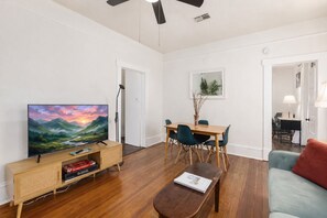 Ein Wohnzimmer mit Flachbildfernseher, Holzmöbeln, einem Esstisch mit Stühlen und einer kleinen Couch.