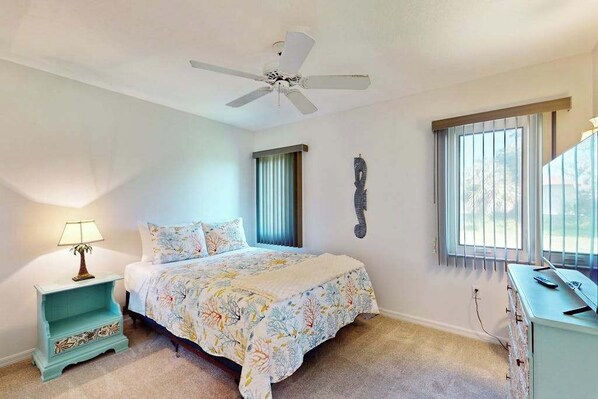 A bedroom with a bed, a ceiling fan, a nightstand, a dresser, a window with blinds, and a wall decoration. - Coastal home on golf course w/ water view, private pool & spa, AC, W/D, Wifi (Rotonda West)
