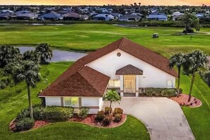 A single-story house with a sloped roof, a front porch, and a driveway leading to the entrance. - Coastal home on golf course w/ water view, private pool & spa, AC, W/D, Wifi (Rotonda West)