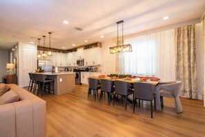A modern kitchen with white cabinets, a central island, and a dining area with a wooden table and chairs. - Stupendous Disney Vacation Home W Private Pool (Kissimmee)