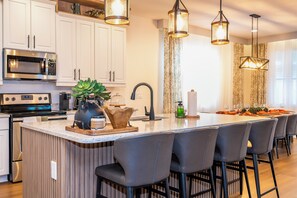A modern kitchen with white cabinetry, a built-in microwave, a coffee maker, and a large island with bar stools. - Stupendous Disney Vacation Home W Private Pool (Kissimmee)