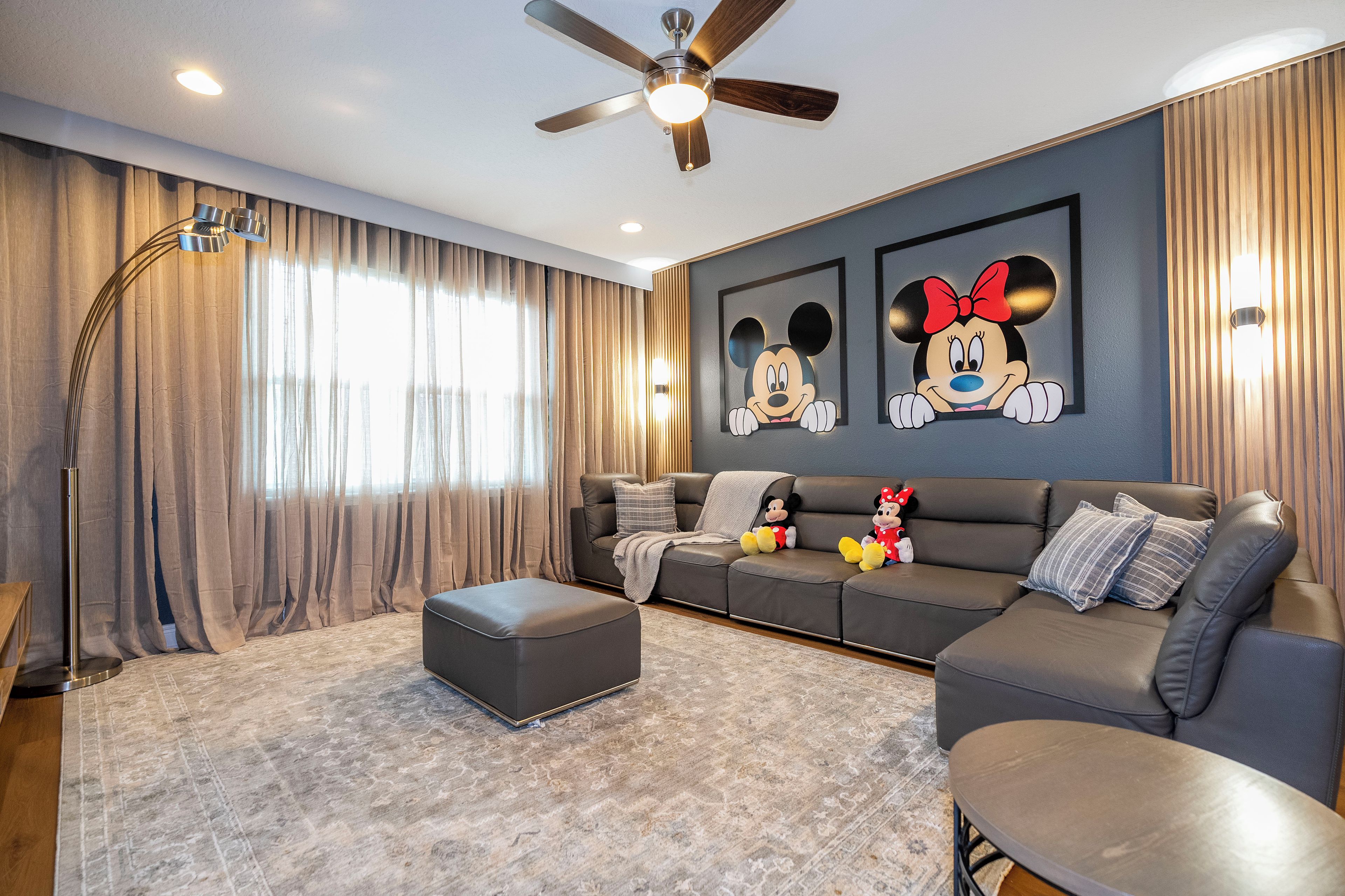 A living room with a ceiling fan, a sofa, an ottoman, and two Mickey Mouse wall art pieces.