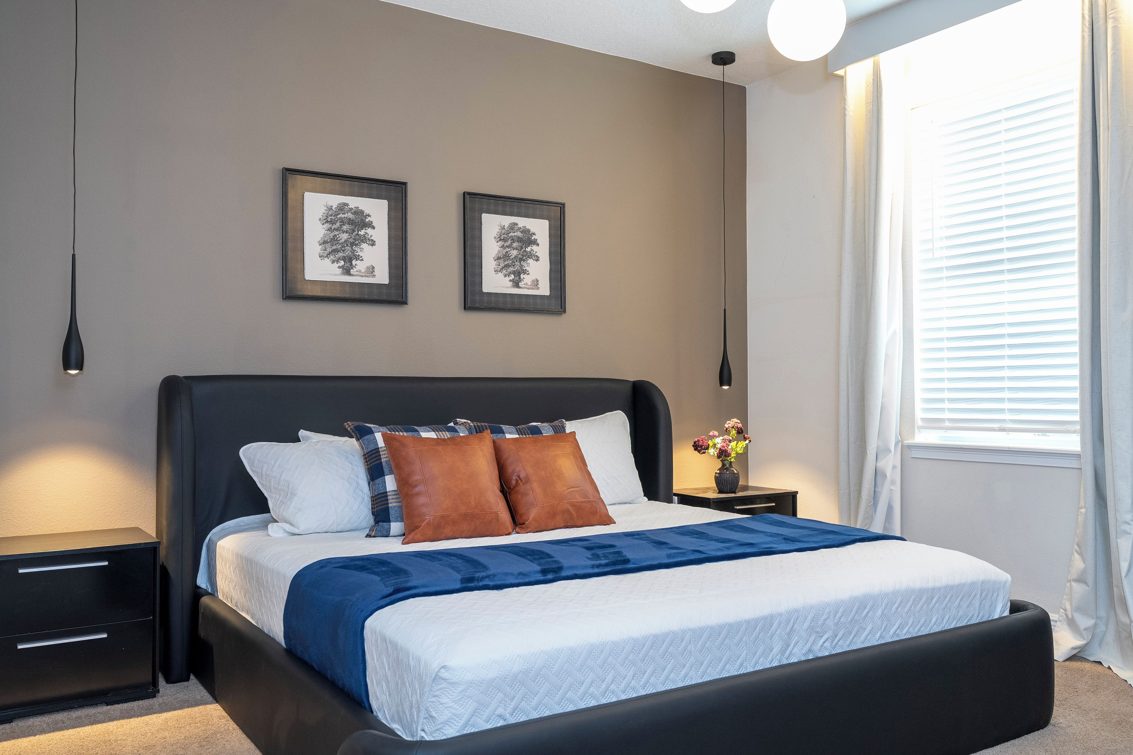 A modern bedroom with a large bed, two bedside tables, a nightstand, a vase with flowers, and two framed pictures on the wall.