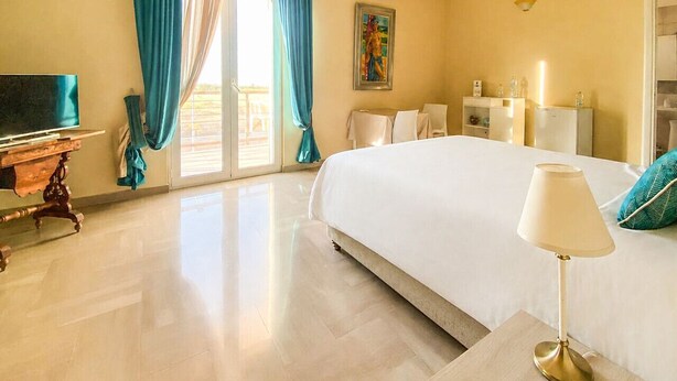 A hotel room with a large bed, a desk with a lamp, a television, and a painting on the wall. - Blue Room - Double Room with Private Garage (Bitonto)