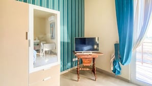 A room with a wooden desk, a television, a wardrobe, and a window with curtains. - Blue Room - Double Room with Private Garage (Bitonto)