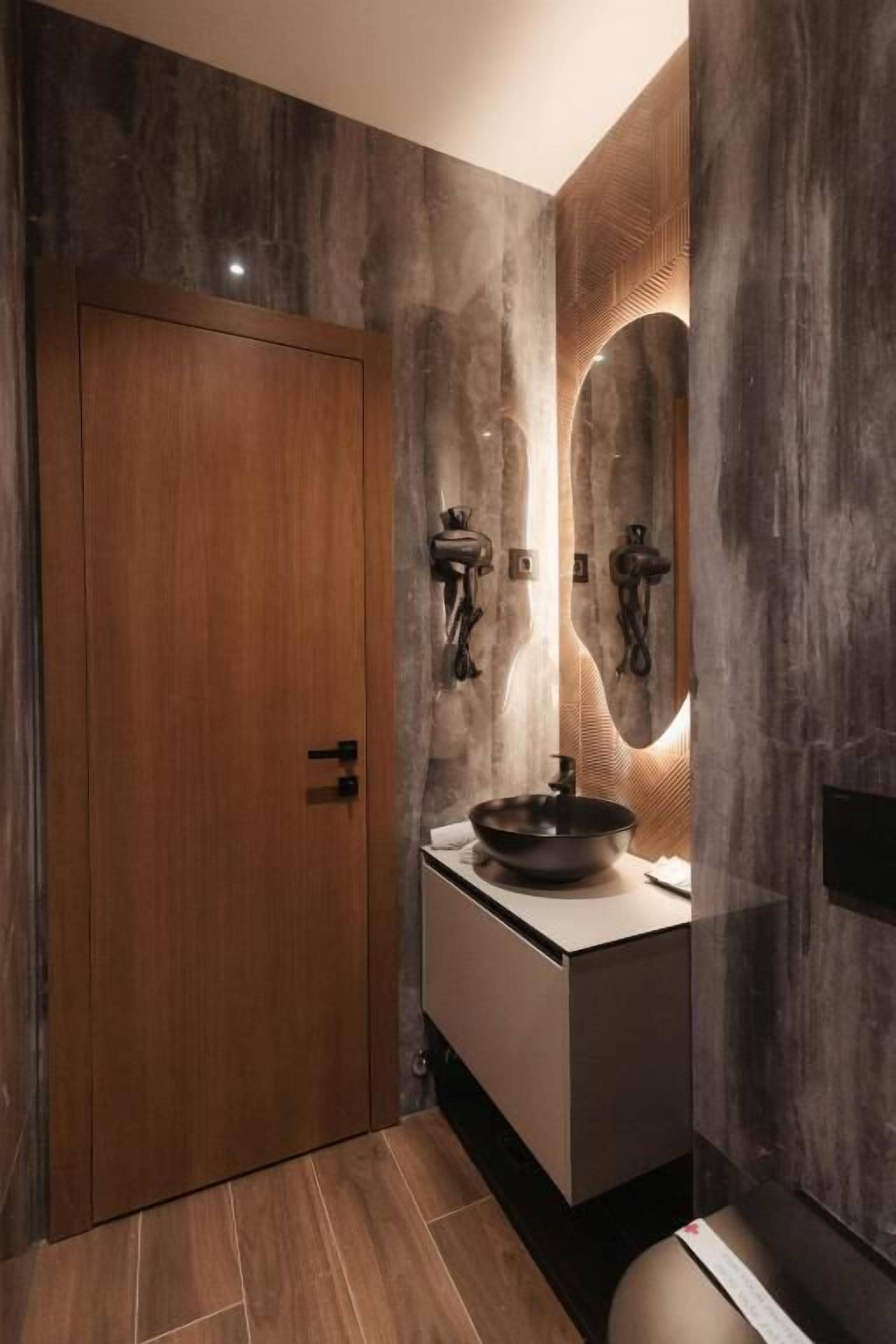 A bathroom with a wooden door, a sink with a basin, and a mirror with a textured wall behind it.