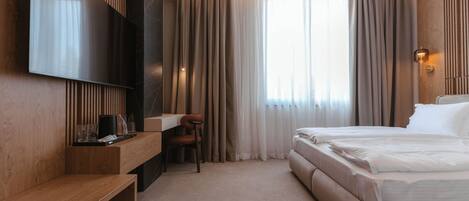 A modern hotel room with a bed, a desk, a chair, and a TV mounted on the wall.