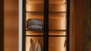 A wooden wardrobe with illuminated shelves, a hanging robe, and a folded towel. - TRADICIJA HOTEL (Banja Luka)
