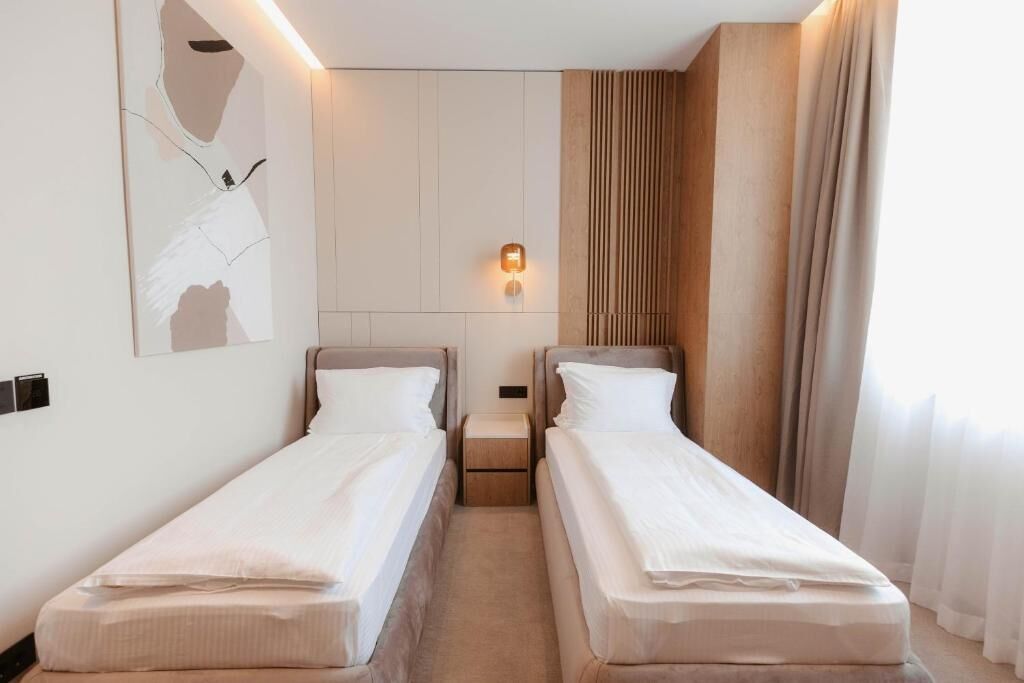 A hotel room with two single beds, a wall-mounted light, and a large abstract painting.