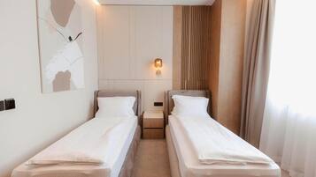 A hotel room with two single beds, a wall-mounted light, and a large abstract painting.