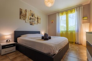 Een slaapkamer met een bed, nachtkastje, wanddecoratie, gordijnen en een raam.
