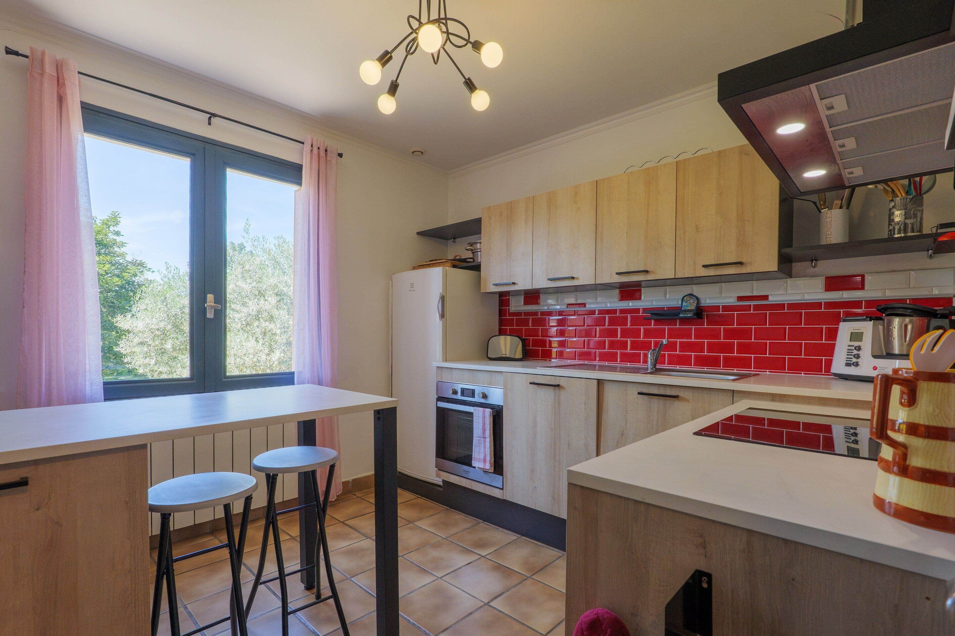 A kitchen with a window, wooden cabinets, a white countertop, and a red-tiled backsplash.