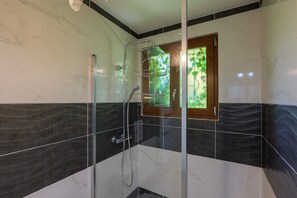A modern bathroom with a glass-enclosed shower, marble tiles, and a view of greenery through a window. - Villa Bella Heated Pool & Garden Family Holiday Home with Wi-Fi (Aubenas)