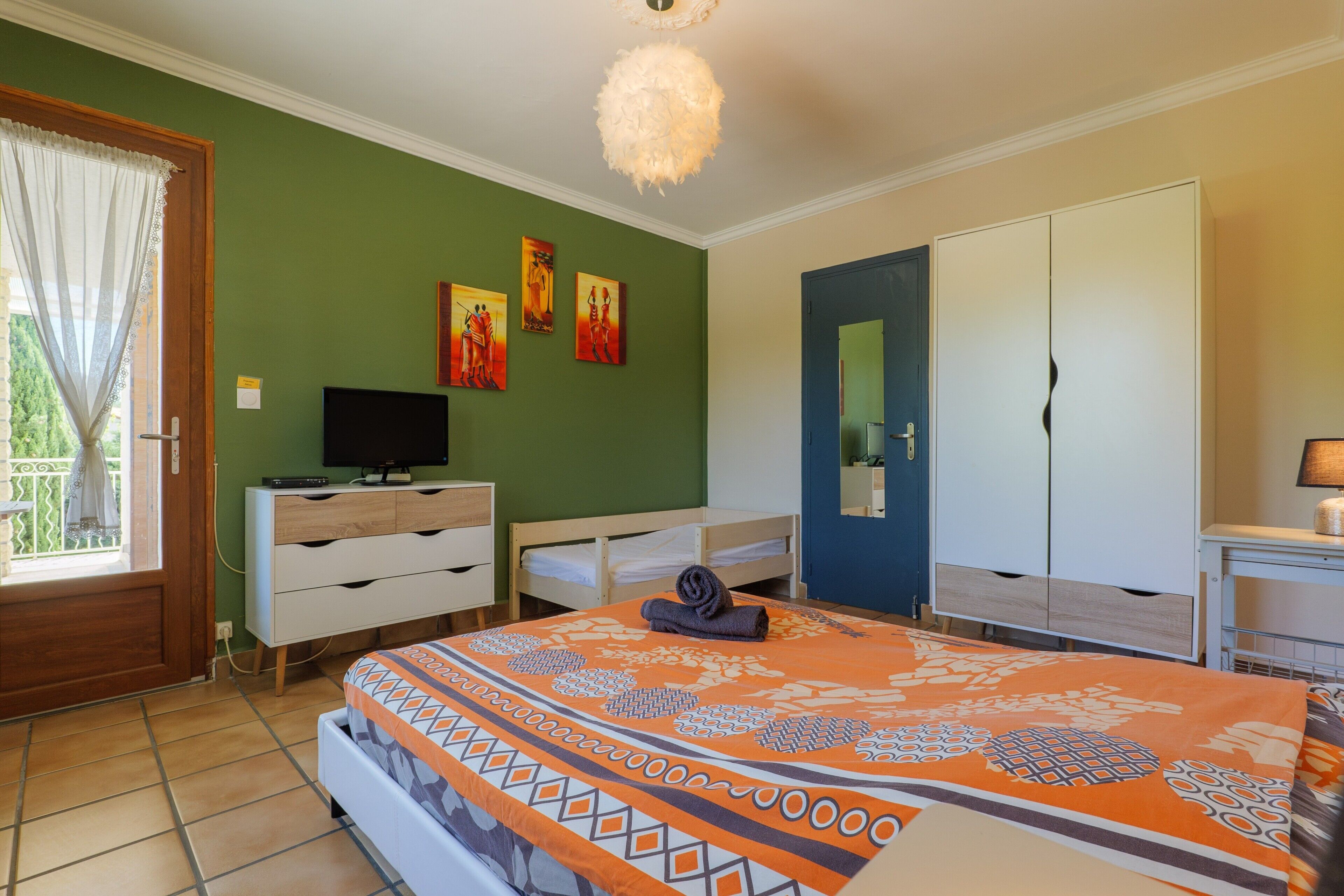 Une chambre à coucher comprenant un lit, une commode, un téléviseur, des œuvres d’art, une armoire et une porte.