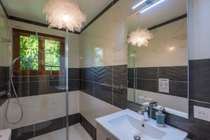 Een moderne badkamer met een douchecabine van glas, een witte wastafel en een grote spiegel.