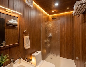 A wooden-paneled bathroom with a glass shower enclosure, a sink, and a towel rack. - The Chapter Stay - Kedarnath (Ukhimath)