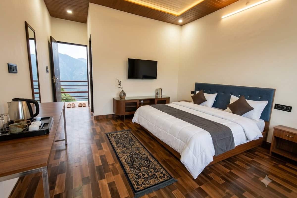 Quarto moderno com uma cama grande, piso de madeira, televisão de tela plana e vista para montanhas.