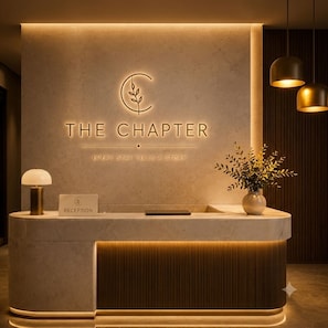 Ein Empfangsschalter mit einem Schild, auf dem 'THE CHAPTER' steht, und dem Slogan 'JEDER AUFENTHALT ERZÄHLT EINE GESCHICHTE'.