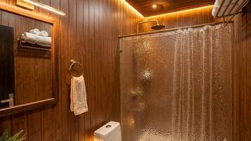 Ein Badezimmer mit Holzwandverkleidung, einer Glasdusche, einem Waschbecken und einem Handtuchhalter.