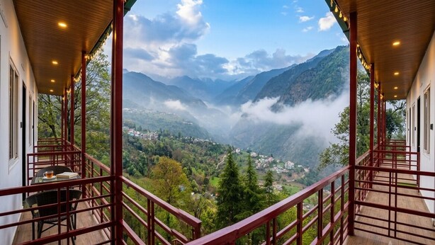 A balcony with a wooden floor and red railings, overlooking a valley with mountains and mist.