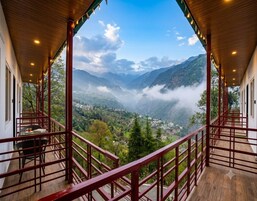 A balcony with a wooden floor and red railings, overlooking a valley with mountains and mist.
