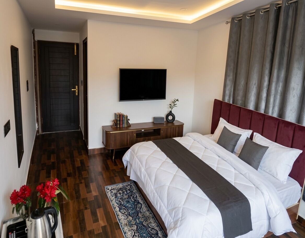 A hotel room with a large bed, a flat-screen TV, a wooden dresser, and a patterned rug.