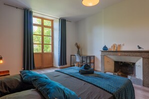 Ein Schlafzimmer mit Bett, Schreibtisch, Stuhl, Kamin und einem fenster mit Vorhängen.